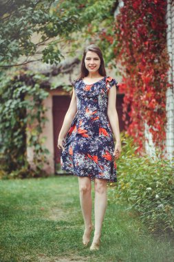 Gülümseyen genç esmer kadın bir elbise onun yurdunda avlusunda poz sevinir, mutlu kaygısız