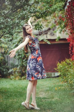 Gülümseyen genç esmer kadın bir elbise onun yurdunda avlusunda poz sevinir, mutlu kaygısız