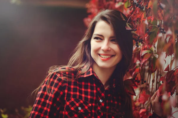 Sonriente joven morena posando en el patio de su residencia en una camisa a cuadros rojo es feliz, retrato feliz despreocupado, salud en tonos cómodos — Foto de Stock