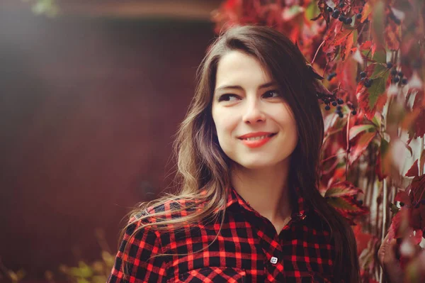 Sonriente joven morena posando en el patio de su residencia en una camisa a cuadros rojo es feliz, retrato feliz despreocupado, salud en tonos cómodos — Foto de Stock