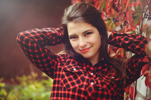 Sonriente joven morena posando en el patio de su residencia en una camisa a cuadros rojo es feliz, retrato feliz despreocupado, salud en tonos cómodos — Foto de Stock