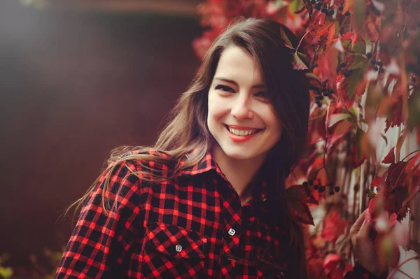 Uśmiechający się młoda kobieta brunetka stwarzające na dziedzińcu jej pobytu w czerwoną koszulę w kratkę jest szczęśliwy, zadowolony zdrowie beztroski, portret w miękkie dźwięki — Zdjęcie stockowe