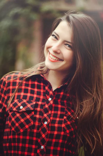 Sonriente joven morena posando en el patio de su residencia en una camisa a cuadros rojo es feliz, retrato feliz despreocupado, salud en tonos cómodos — Foto de Stock