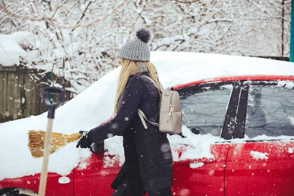 Winterporträt einer jungen Frau, die Schnee von einem Auto räumt. Die schöne Blondine lacht und putzt fröhlich den Schnee. schöne junge Frau im Freien — Stockfoto