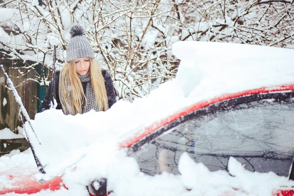 Winterporträt einer jungen Frau, die Schnee von einem Auto räumt. Die schöne Blondine lacht und putzt fröhlich den Schnee. schöne junge Frau im Freien — Stockfoto