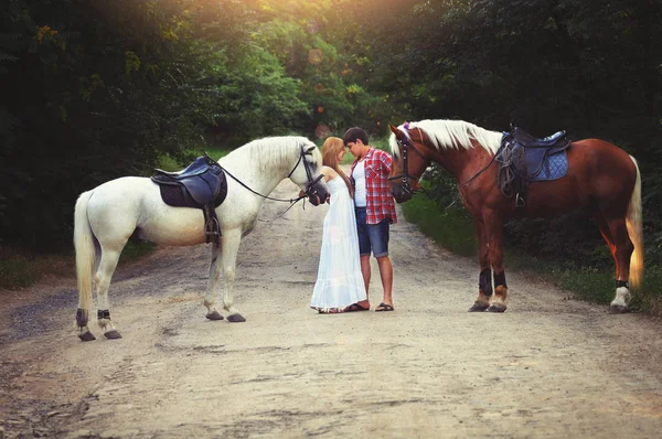 Belo casal amoroso com cavalos ficar na floresta na estrada, imagem artística acolhedora e quente, voando dia brilhante — Fotografia de Stock