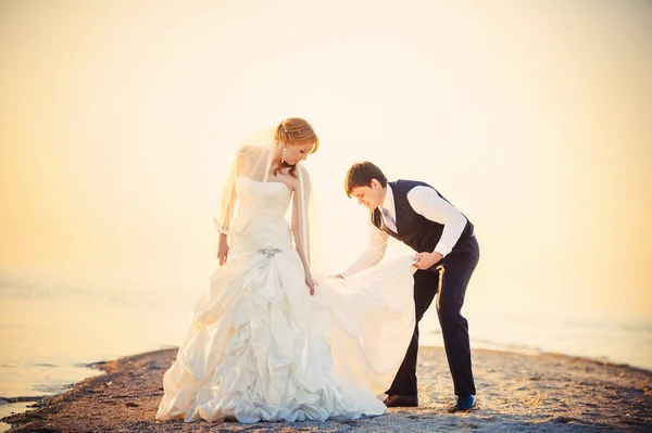 Para ślub na plaży o zachodzie słońca, człowiek w kamizelce dostosowuje się do sukni, ciepłe i przytulne obrazu — Zdjęcie stockowe