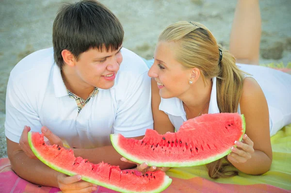 Feliz casal amoroso em um piquenique comendo uma melancia em roupas brancas na praia, um dia ensolarado de férias — Fotografia de Stock