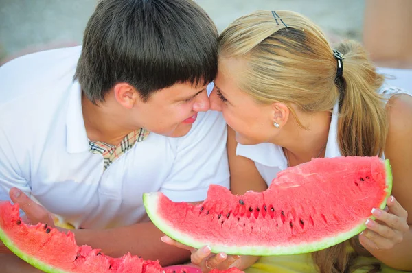 Feliz casal amoroso em um piquenique comendo uma melancia em roupas brancas na praia, um dia ensolarado de férias — Fotografia de Stock