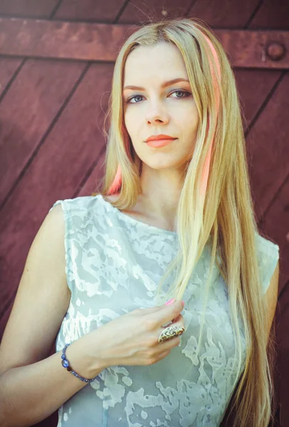 Femme blonde sur un fond en bois rouge a ses cheveux peints dans une bande rayée rose, timide et curieuse — Photo