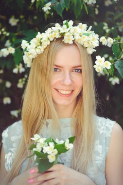 Yasemin ile sarışın çekici mütevazı genç kızla çelenk uzun kafa saç ve açık havada beyaz elbise, hassasiyet ve yumuşaklık doğa arka plan üzerinde doğal makyaj çiçekler