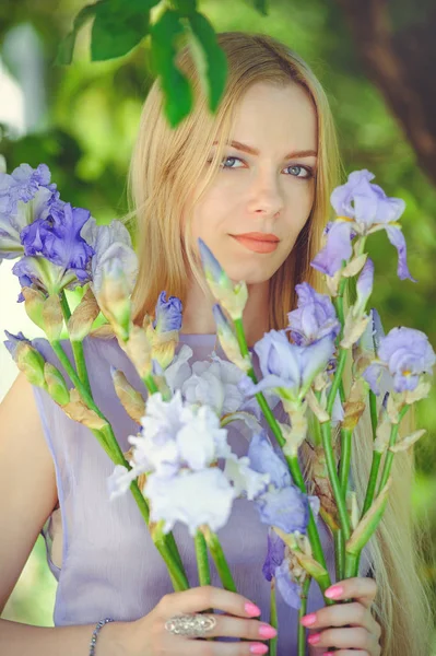 Çekici kızı sarışın dren saç ve doğal makyaj bir arka plan açık havada, hassasiyet ve yumuşaklık bir doğa zemin üzerine mavi mor Iris çiçek kokulu — Stok fotoğraf