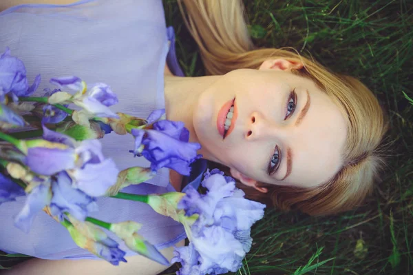 Atrakcyjna, młoda dziewczyna z dr blond włosy i makijaż naturalny, pachnące kwiaty niebieskie irysy, leżącego na trawie, na zewnątrz, tkliwość i miękkość na tle przyrody — Zdjęcie stockowe