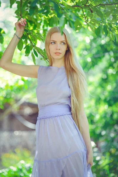 Attractive modest young girl with blond dren hair and natural make-up in purple dress outdoors, tenderness and softness on nature background