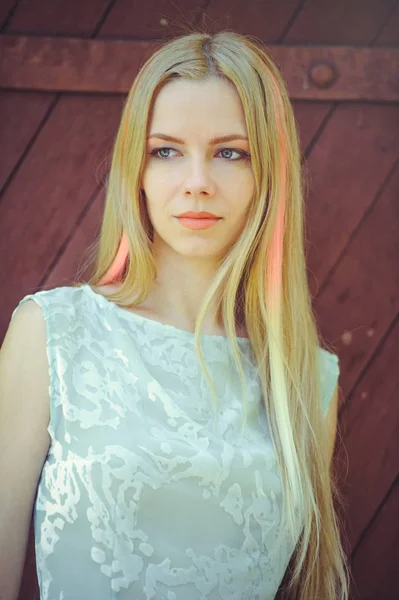 Ελκυστική μέτρια νεαρή ξανθιά γυναίκα σε κόκκινο φόντο ξύλινη τα μαλλιά της βαμμένα σε ροζ ριγέ ριγέ, σε μπλε φόρεμα ντροπαλός και περίεργο — Φωτογραφία Αρχείου