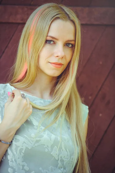 Привлекательная скромная молодая блондинка на красном деревянном фоне ее волосы окрашены в розовую полосатую полоску, в голубое платье застенчиво и любознательно — стоковое фото