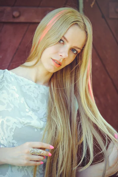 Mulher loira modesta atraente no fundo de madeira vermelho seu cabelo pintado em listrado listrado rosa, em vestido azul tímido e curioso — Fotografia de Stock