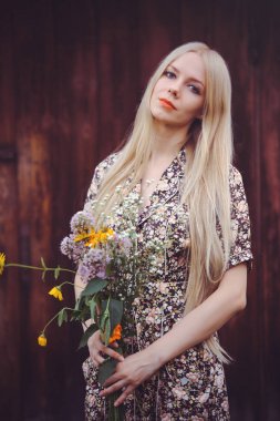 Mary'e yaz aylarında güzel genç kadın elbise kırmızı eski ahşap zemin üzerine, kameraya bakıyor. rustik tarzı oldukça ile kır çiçekleri elinde