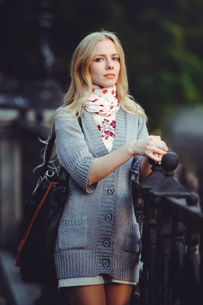 Beautiful blond woman standing in the city at night dressed in a white dress and a sweater on her neck scarf, modest and shy, — Stock Photo, Image