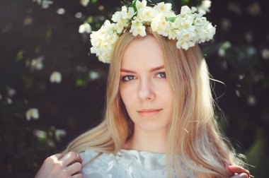 Yasemin ile sarışın çekici mütevazı genç kızla çelenk uzun kafa saç ve açık havada beyaz elbise, hassasiyet ve yumuşaklık doğa arka plan üzerinde doğal makyaj çiçekler