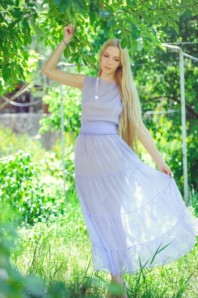 Attractive modest young girl with blond  hair and natural make-up in purple dress outdoors, tenderness and softness on nature background