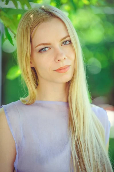 Attractive modest young girl with blond  hair and natural make-up in purple dress outdoors, tenderness and softness on nature background