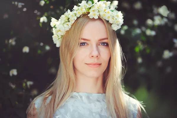 Muchacha joven atractiva modesta con rubia con flores de jazmín corona en la cabeza pelo largo y maquillaje natural en vestido blanco al aire libre, ternura y suavidad en el fondo de la naturaleza — Foto de Stock