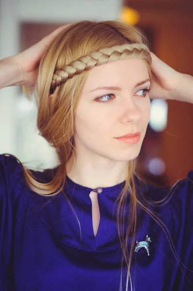 Bonita mujer rubia con el pelo trenzado jugando, las manos en la cabeza vestida con un vestido azul, hermoso retrato en la casa, imagen casera simple, cuidado del cabello — Foto de Stock