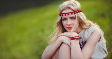 ihale sarışın kadın başına, şık ve rahat yeşil bir arka plan üzerinde bir doğal işlemeli elbise bandaj giymiş çimlerin üzerine oturur. Aşk reklam panoramik bir kavramdır. metin için yer.