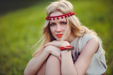 ihale sarışın kadın başına, şık ve rahat yeşil bir arka plan üzerinde bir doğal işlemeli elbise bandaj giymiş çimlerin üzerine oturur. Doğa sevgisi reklam kavramı. metin için yer.