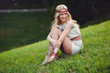 ihale sarışın kadın başına, şık ve rahat yeşil bir arka plan üzerinde bir doğal işlemeli elbise bandaj giymiş çimlerin üzerine oturur. Doğa sevgisi reklam kavramı. metin için yer.