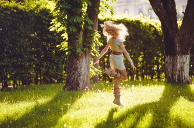 ihale kadın sarışın yürüyüşler karşı doğal bir etnik giyinmiş akşam güneşi fon çimenlerin üzerinde elbise, şık ve rahat. Doğanın aşk kavramı.