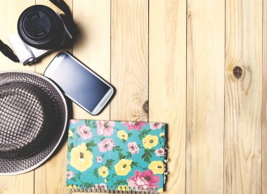 Moda seyahat aksesuarları tahta masada telefon kamera şapka ve defter.