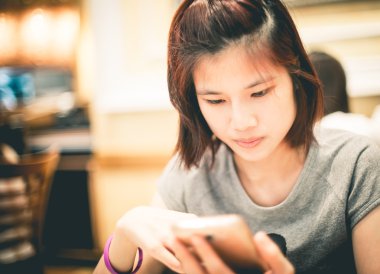 Şirin Asyalı kız kafede bir cep telefonu kullanıyor.