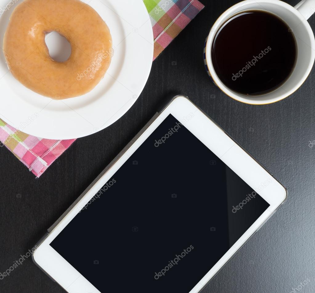 Blank Empty Tablet screen on black cafe table with donut and coffee. Reading tablet on a coffee break table.
