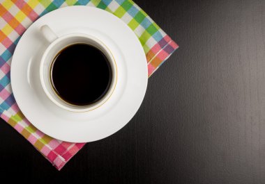 Siyah ahşap masa üzerinde siyah sıcak kahve ile bir beyaz kahve fincanı. Cafe tablo kopya alanı ile renkli yer mat siyah kahve fincanı.