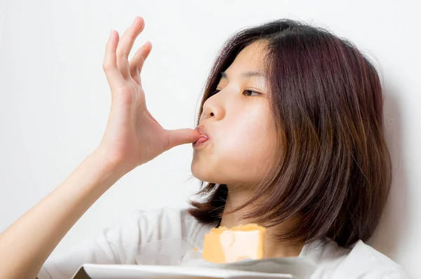 Japonesa chica es profundamente disfrutando por lamer el pastel en su dedo, sobre fondo blanco . — Foto de Stock