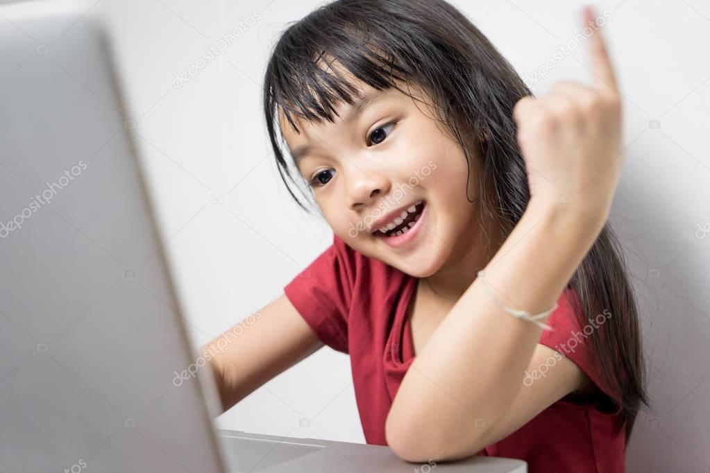 Asian girl is looking very interesting with the content on the computer. Content on the Internet is making little girl very happy. Japanese girl is getting smart and idea from her laptop.