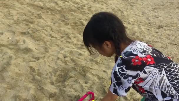 Asiatisk tjej leker med sand hink på stranden — Stockvideo