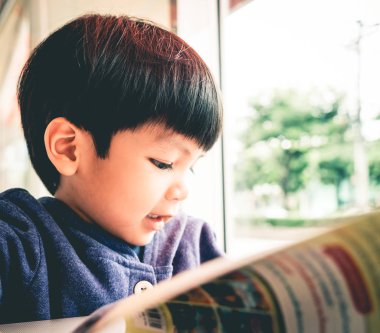 Japon çocuk Cafe windows bir kitap okuyor.