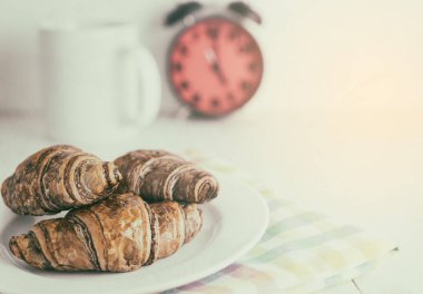 Bir çalar saat ile kahvaltıda çay ile Çikolatalı kruvasan.