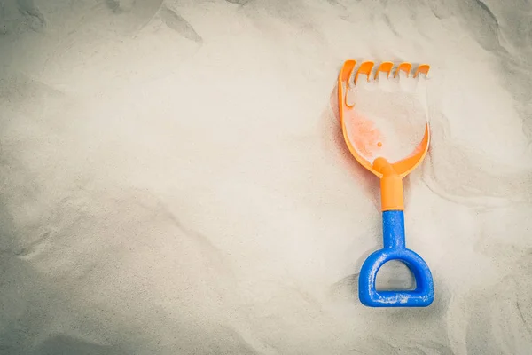 Orange toy shovel in on a clean sand playground with copy space.