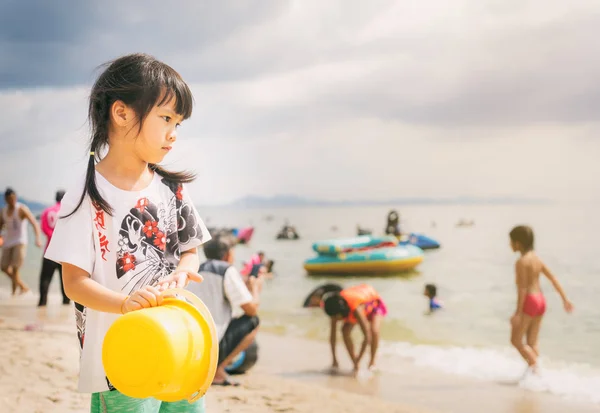 Menina está de pé na praia movimentada olhando para o oceano . — Fotografia de Stock