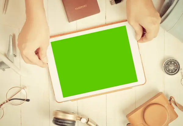 Viaje está sosteniendo la pantalla de tableta en blanco en una mesa llena de accesorios de viaje — Foto de Stock