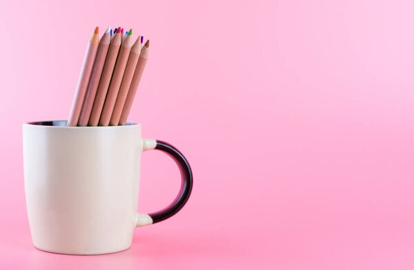 Куча цветных карандашей в кофейной кружке на розовом копировальном пространстве
