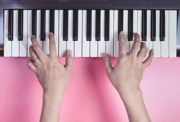 Hand playing Music keyboard on pink background, above view. — Stock Photo, Image