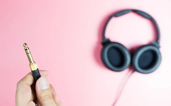 Sostiene conector de auriculares dorados sobre fondo rosa — Foto de Stock