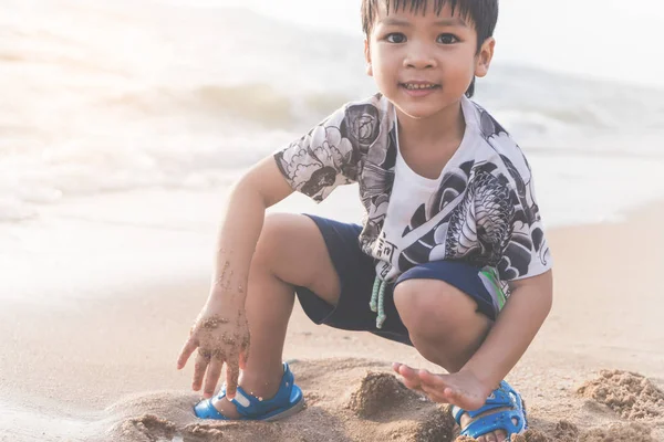 Lycklig pojke leker med sand på en strand — Stockfoto