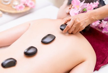 Bir kadın sırt üstünde-e doğru siyah sıcak taş Spa terapisti yerleştirme