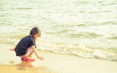 Küçük kız sahilde okyanus dalgası ile oynuyor